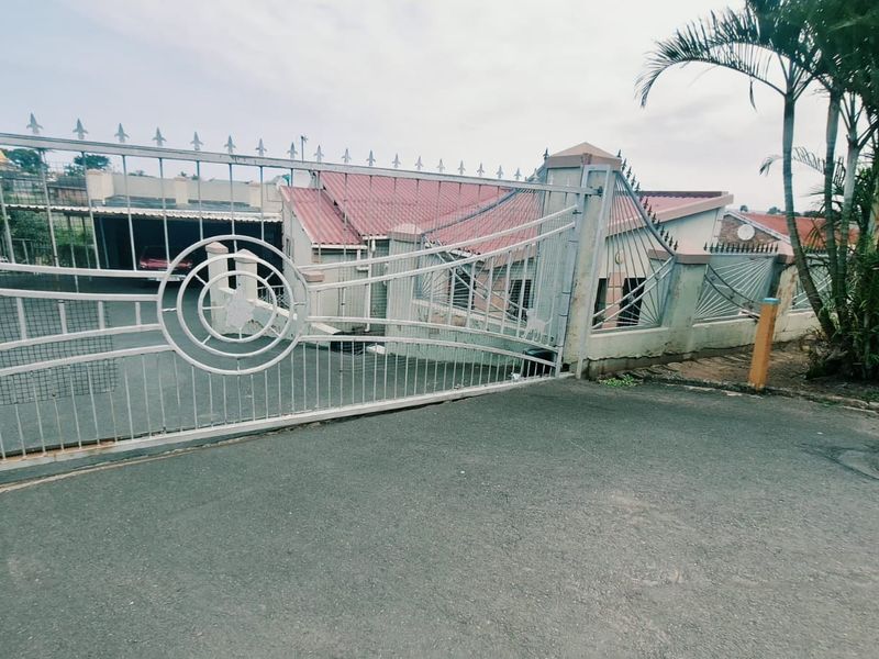 Front view of the property featuring a metal security gate, perimeter wall, and paved driveway leading to the main house structure.