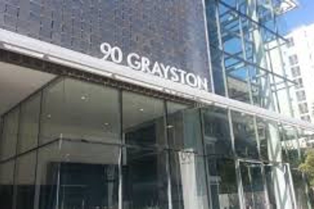 Modern commercial building facade featuring extensive glass curtain walling, steel structural elements, and prominent building signage at the entrance.