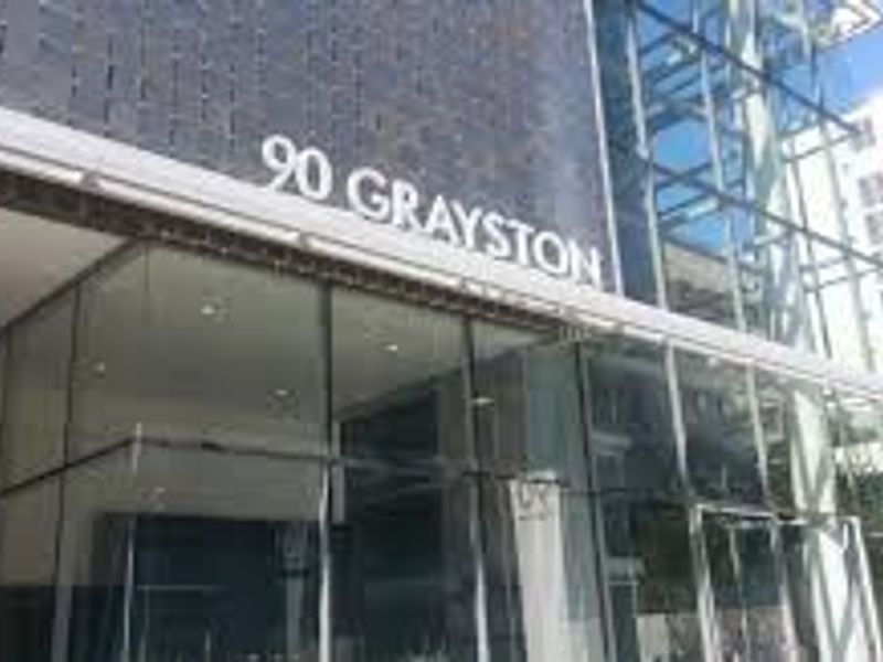 Modern commercial building facade featuring extensive glass curtain walling, steel structural elements, and prominent building signage at the entrance.