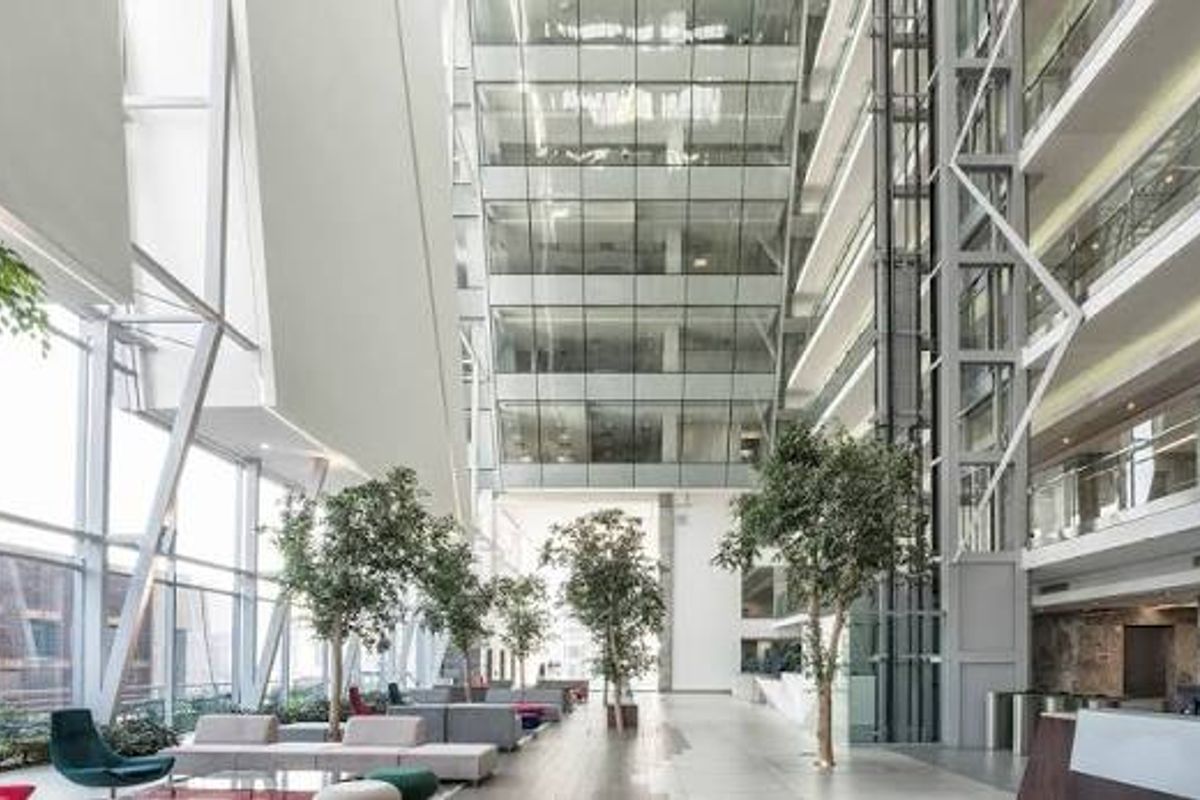 Spacious modern commercial atrium featuring a soaring glass facade, integrated glass elevator, and contemporary architectural steel framing in a high-end office environment.