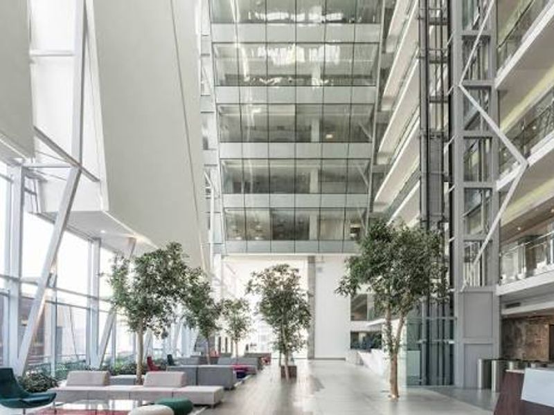 Spacious modern commercial atrium featuring a soaring glass facade, integrated glass elevator, and contemporary architectural steel framing in a high-end office environment.