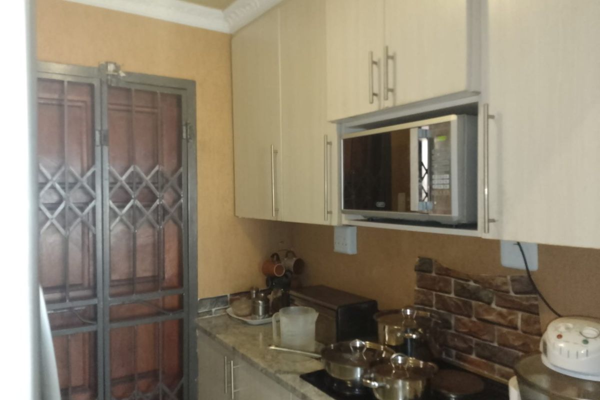 A compact kitchen featuring built-in cabinetry, a stone countertop, a brick-style backsplash, and an integrated microwave, with a security gate at the entrance.