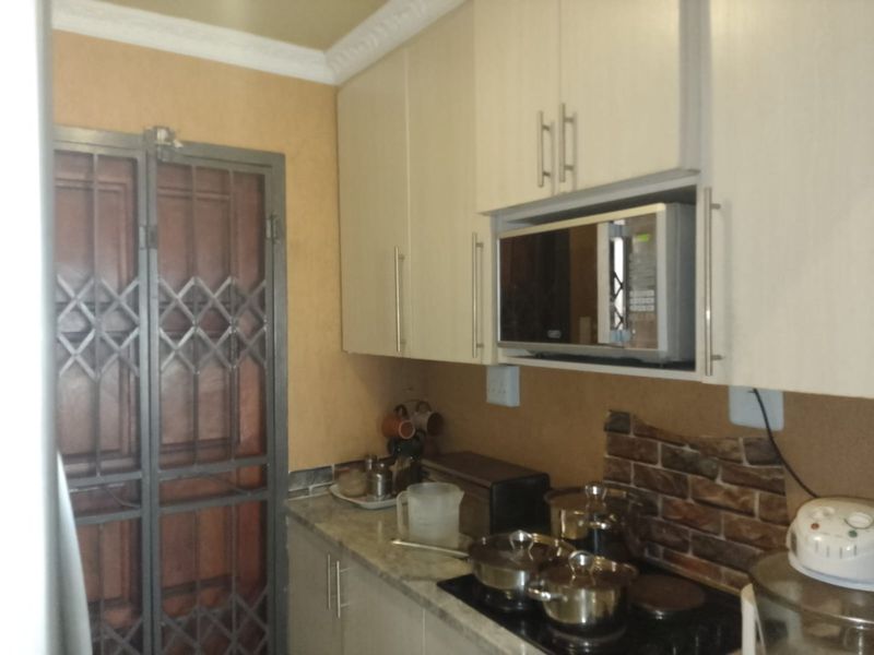 A compact kitchen featuring built-in cabinetry, a stone countertop, a brick-style backsplash, and an integrated microwave, with a security gate at the entrance.