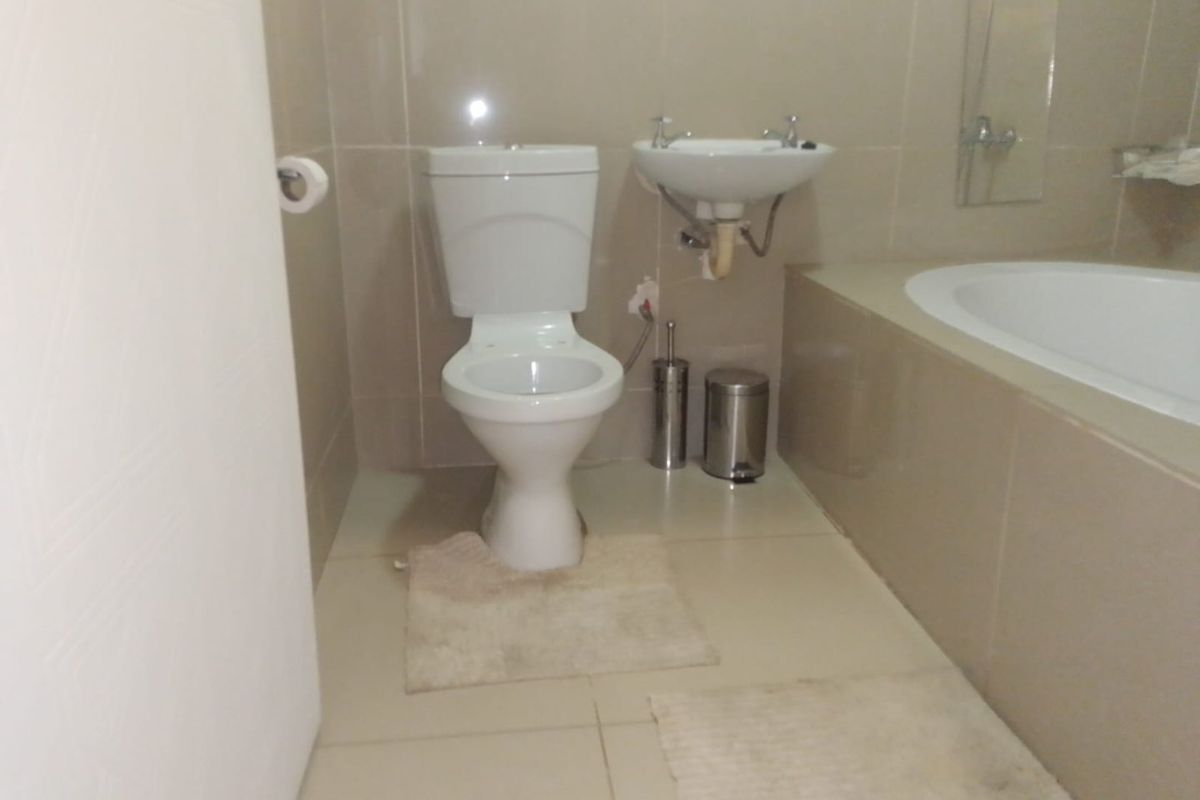 A functional bathroom featuring a built-in bathtub, wall-mounted basin, and toilet with neutral wall and floor tiling.