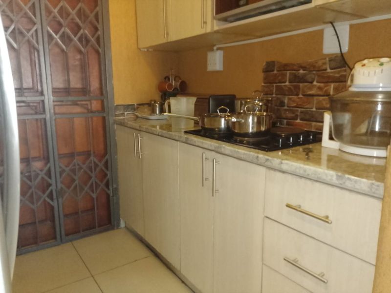 Compact kitchen featuring light-toned cabinetry, stone-look countertops, a brick-style splashback, and a secure entrance door.