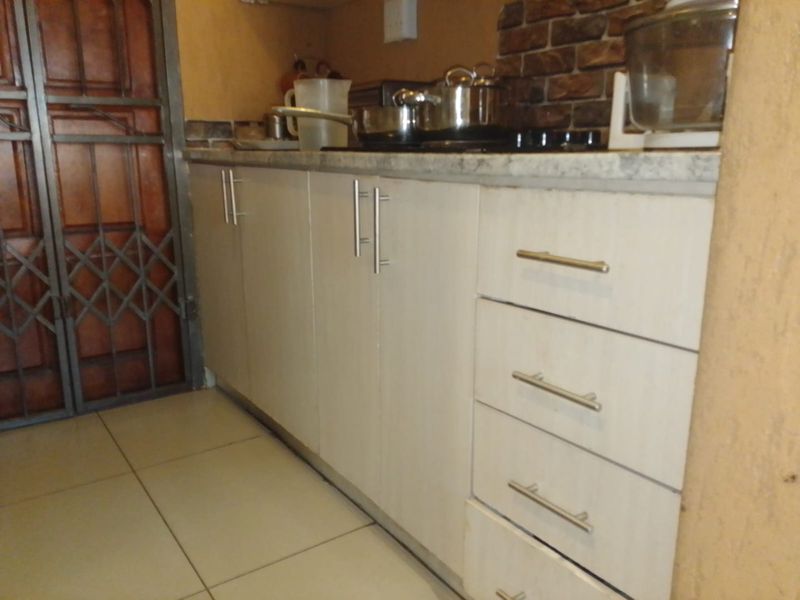 A compact kitchen area featuring white built-in cabinetry, a laminate countertop with an integrated hob, and tiled flooring.