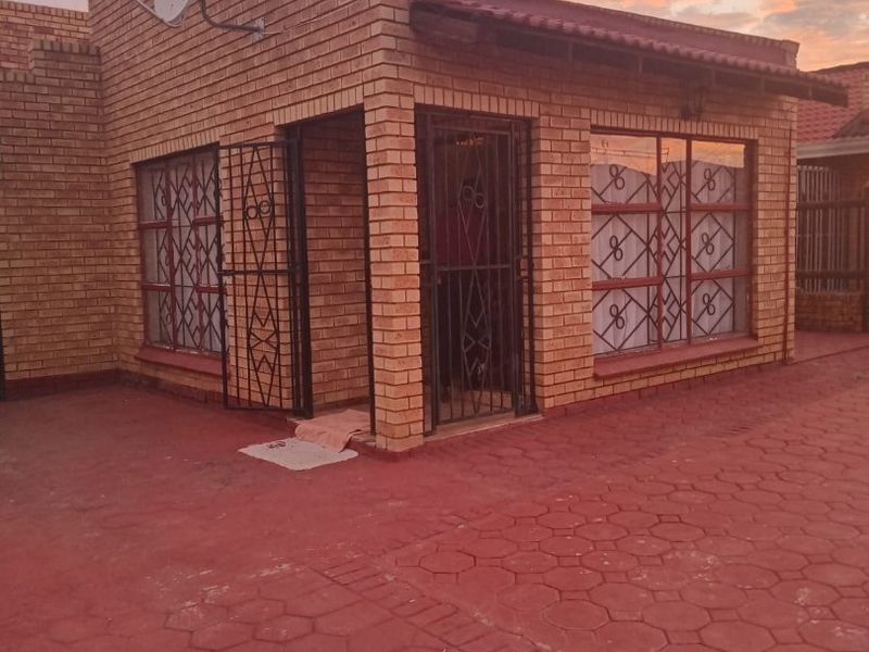 A face brick residential property featuring security gates, window bars, and a paved driveway, captured during sunset.