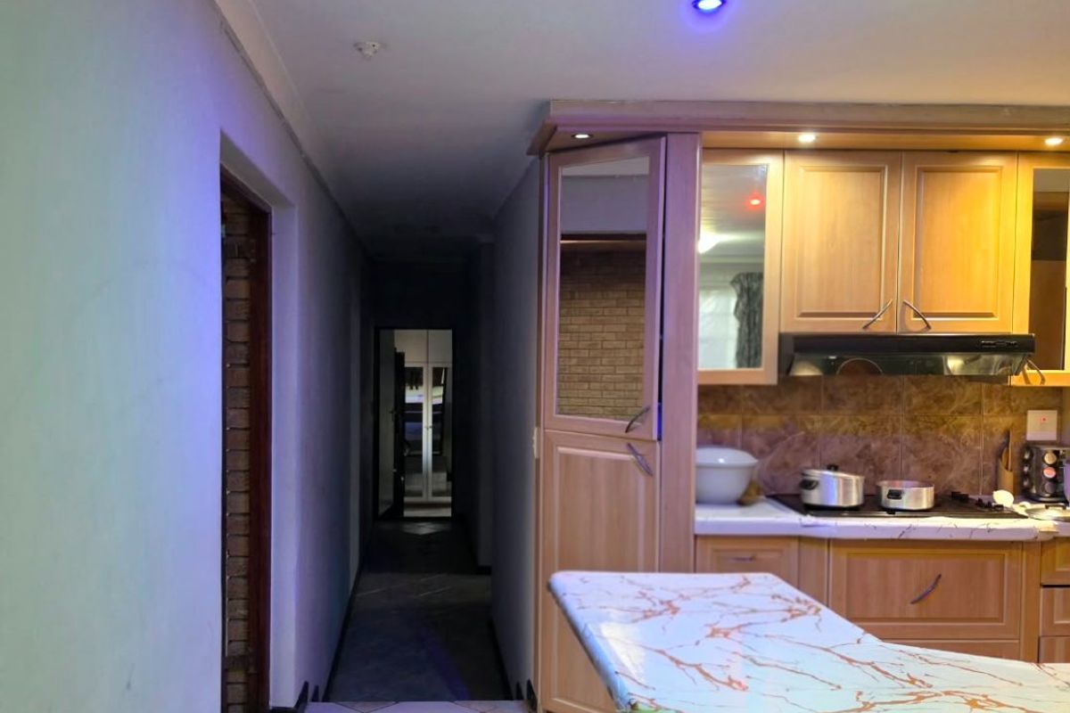 A kitchen area featuring wooden cabinetry, a marble-look breakfast bar, and tiled flooring, leading into a hallway.