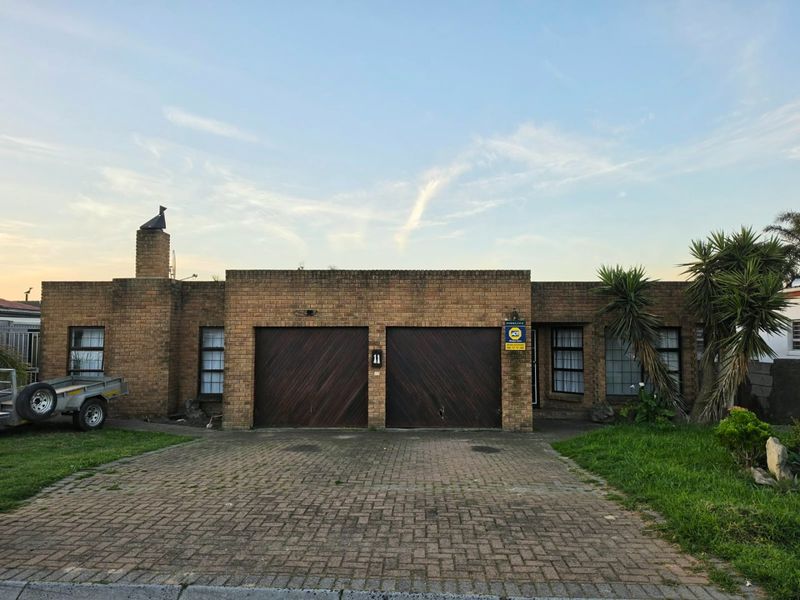 Front elevation of a single-story brick house featuring a double garage, paved driveway, and a prominent chimney.