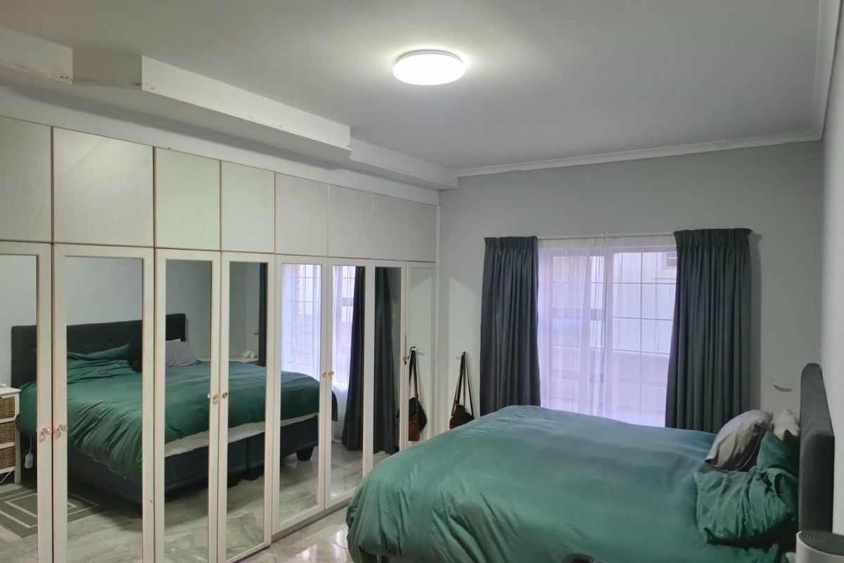 A bedroom featuring extensive built-in mirrored wardrobes, tiled flooring, and a central ceiling light fixture.