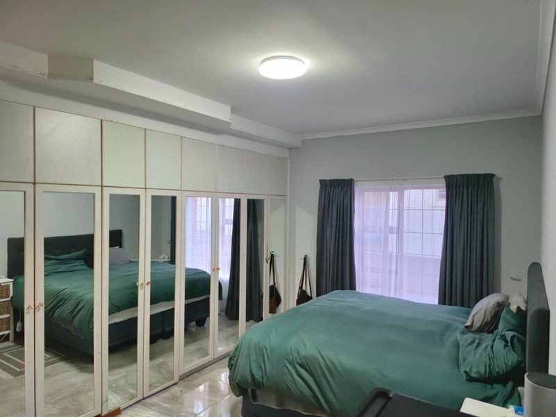 A bedroom featuring extensive built-in mirrored wardrobes, tiled flooring, and a central ceiling light fixture.