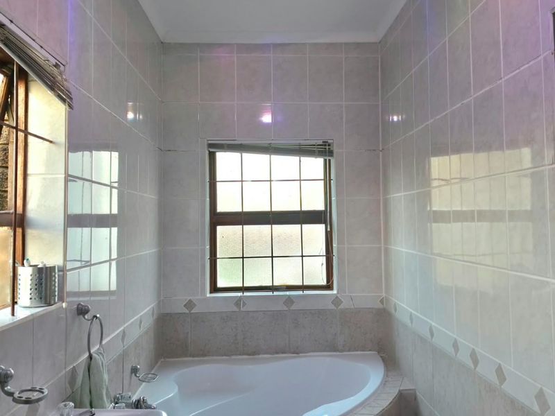 A functional bathroom featuring a corner bathtub, pedestal basin, and full-height wall tiling with a neutral finish.