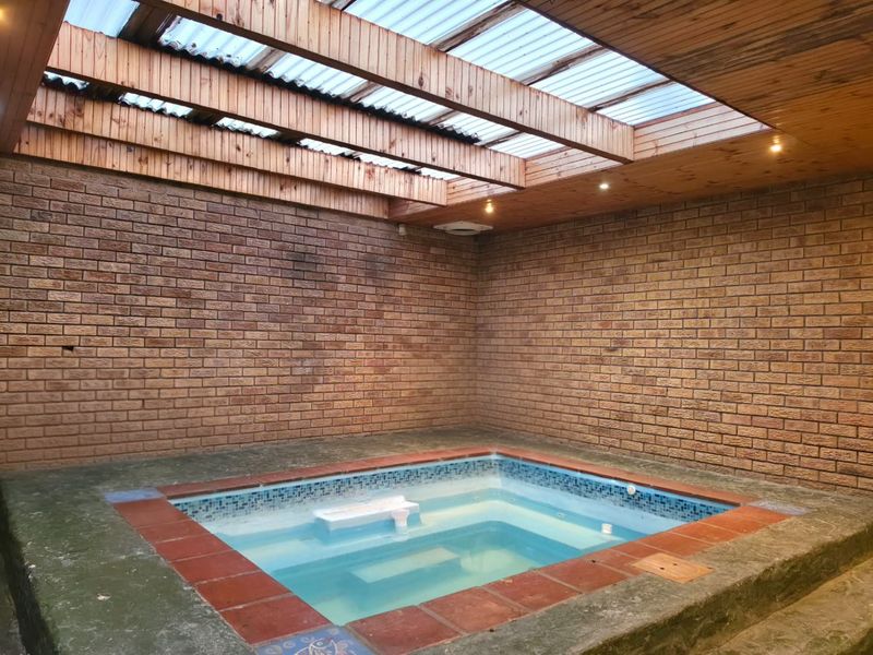 An indoor pool area featuring exposed brick walls, a timber-beamed ceiling with translucent panels, and recessed lighting, providing a private swimming space.
