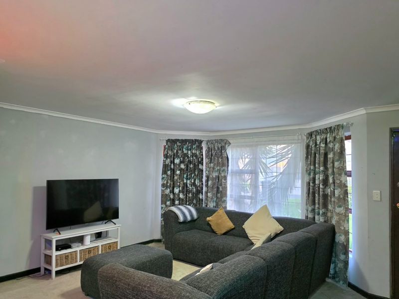 A living room featuring a large window with curtains, ceiling cornice, and a central flush mount light fixture.