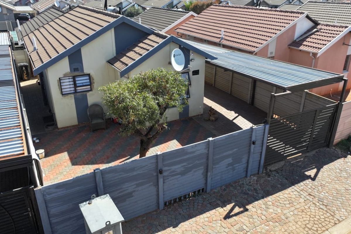 Aerial view of a residential property featuring a tiled roof, paved driveway, carport, and secure boundary walling.