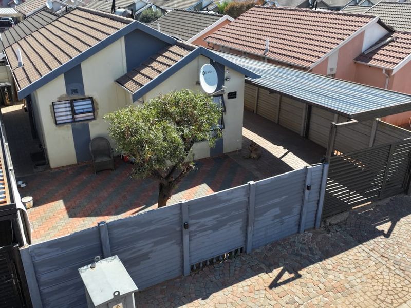 Aerial view of a residential property featuring a tiled roof, paved driveway, carport, and secure boundary walling.