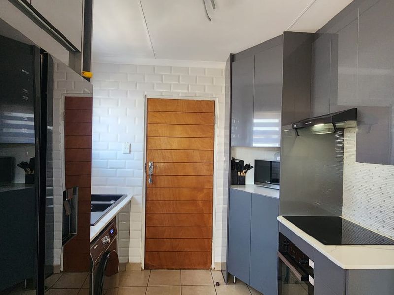 Modern kitchen featuring sleek grey cabinetry, built-in oven and hob, subway tile backsplash, and tiled flooring with a solid wood door.