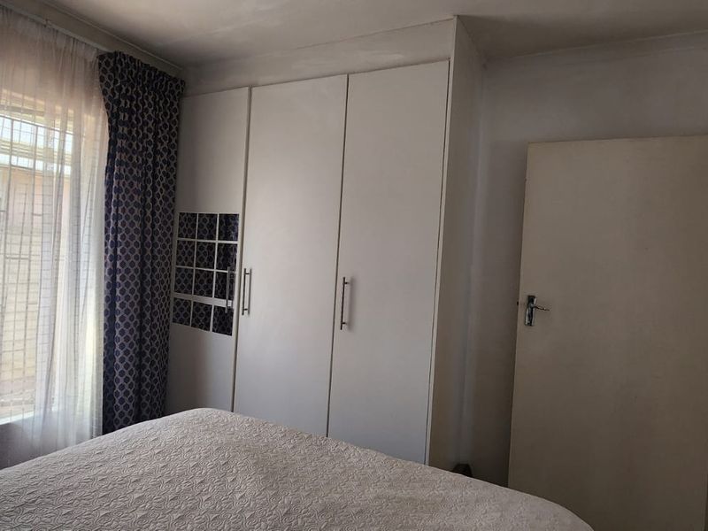 A functional bedroom featuring built-in cupboards, security bars on the window, and standard internal door access.