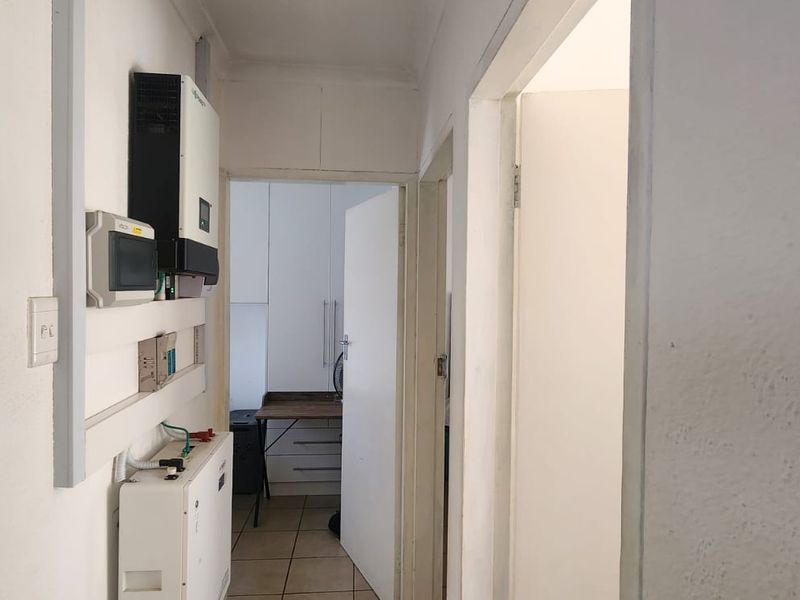 A functional hallway featuring a wall-mounted solar inverter and battery storage system, leading towards a secondary room with built-in cabinetry.