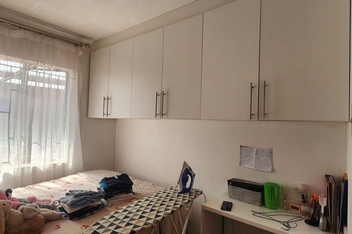 A bedroom featuring built-in overhead storage cupboards and a window allowing natural light.