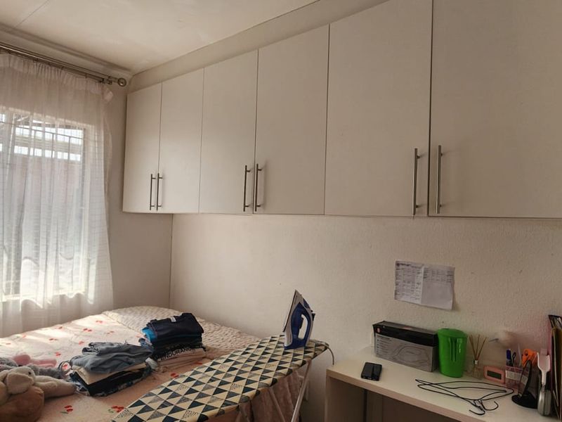A bedroom featuring built-in overhead storage cupboards and a window allowing natural light.