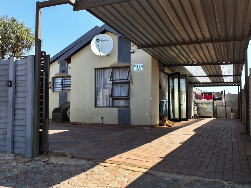 Front exterior view of the house featuring a paved driveway, covered carport, and secure boundary wall with gated access.
