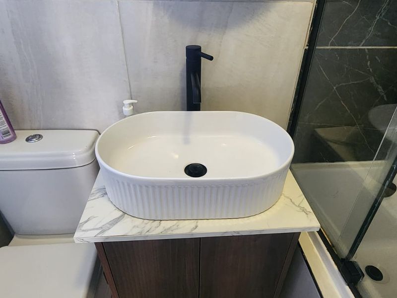 Modern bathroom featuring a vessel sink with a black faucet, marble-look vanity countertop, and a glass-enclosed shower area with tiled finishes.