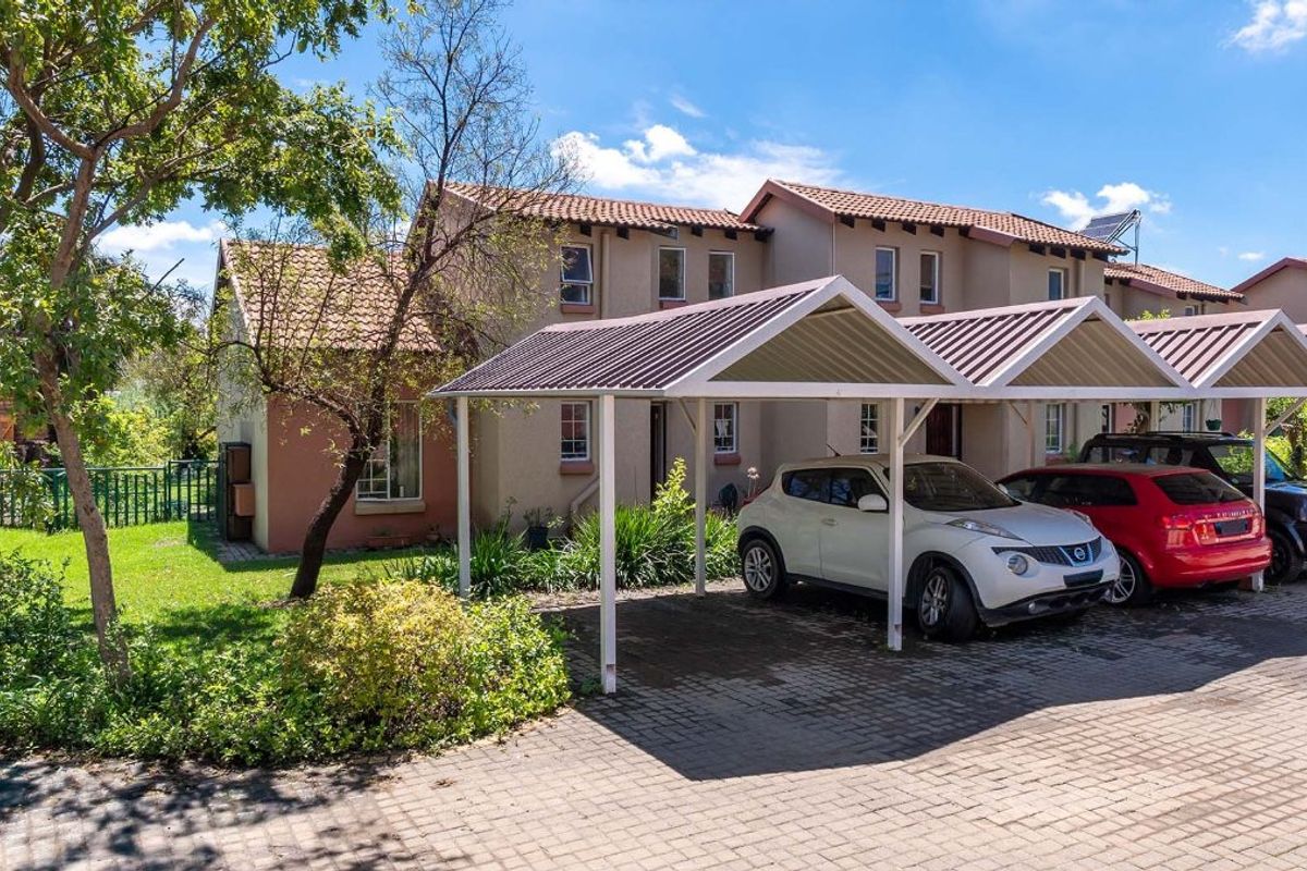 Front exterior view of the apartment complex featuring a paved driveway, covered carports, and established garden landscaping.