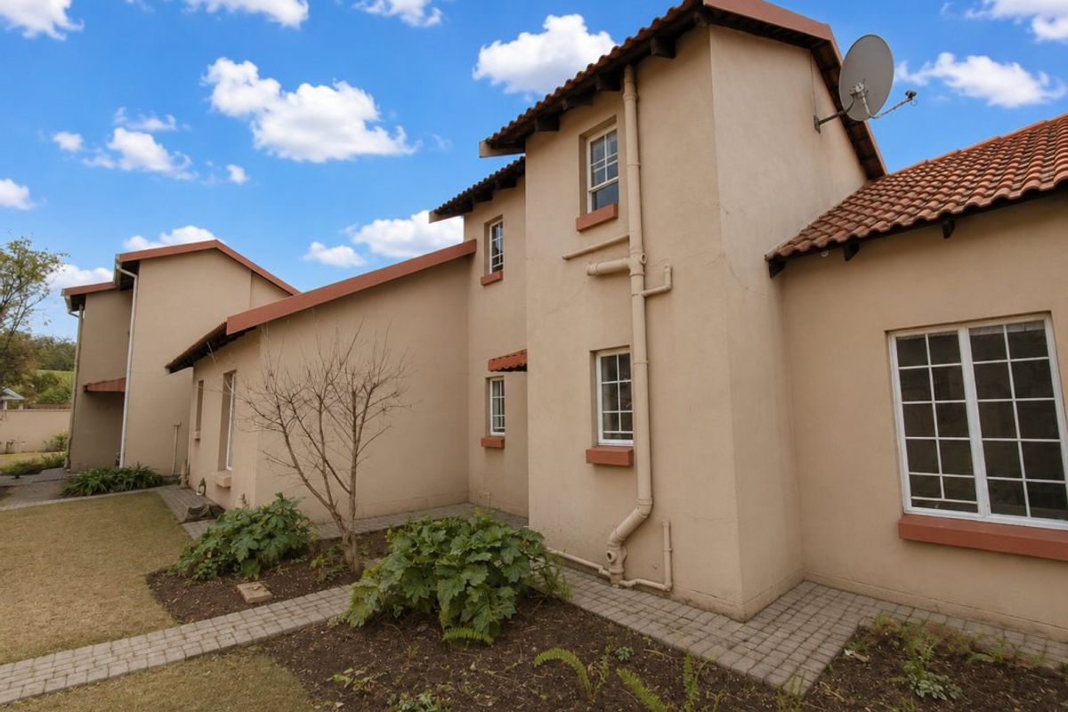 Rear view of the apartment building featuring plastered walls, terracotta roof tiles, paved walkways, and established garden beds.