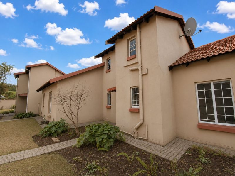 Rear view of the apartment building featuring plastered walls, terracotta roof tiles, paved walkways, and established garden beds.