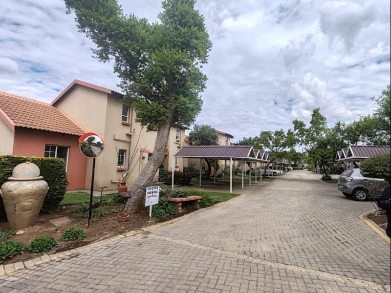 Exterior view of the apartment complex featuring a paved driveway, covered parking bays, and landscaped garden areas.