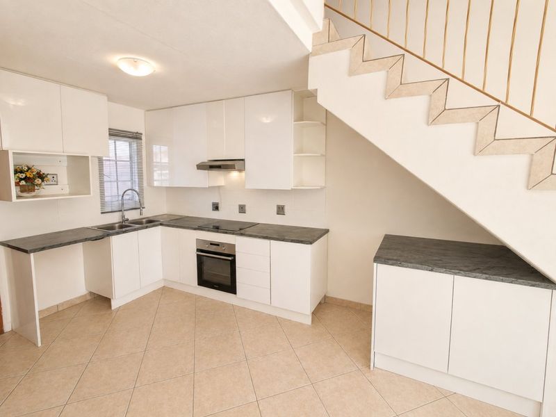 Modern kitchen featuring white cabinetry, dark countertops, integrated oven and hob, and tiled flooring, situated beneath an open staircase.