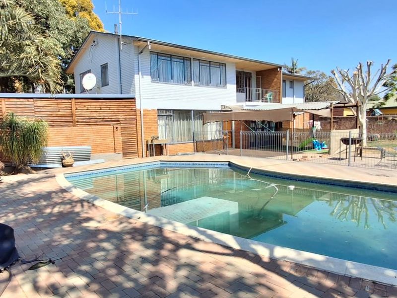 Rear exterior view featuring a swimming pool, paved patio area, and a two-story residential building with a balcony.