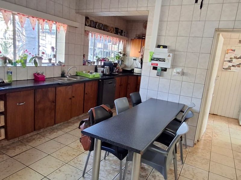A functional kitchen featuring wooden cabinetry, laminate countertops, and full-height wall tiling, offering a practical layout with an adjacent dining area.