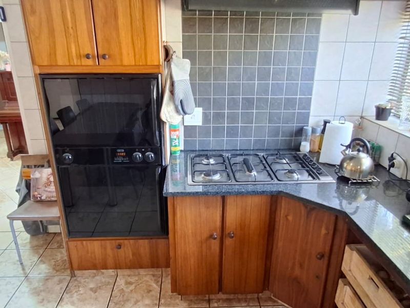 A functional kitchen featuring wooden cabinetry, granite countertops, a built-in oven, and a gas hob with a tiled backsplash.