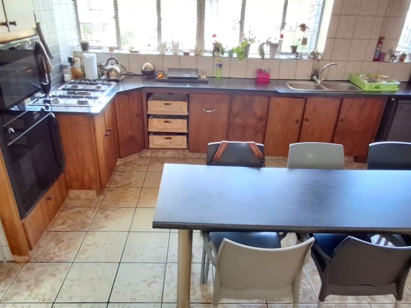 A functional kitchen featuring wooden cabinetry, a gas hob, built-in oven, and tiled finishes, offering a practical layout with an integrated dining area.