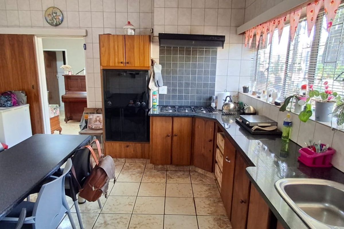 A functional kitchen featuring wooden cabinetry, a gas hob, built-in oven, and tiled finishes, offering a practical layout with potential for modern updates.