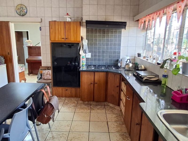 A functional kitchen featuring wooden cabinetry, a gas hob, built-in oven, and tiled finishes, offering a practical layout with potential for modern updates.
