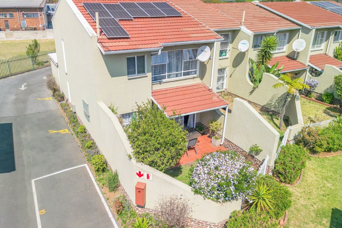 Aerial view of a townhouse featuring a tiled roof with solar panels, a private patio area, and an adjacent driveway.