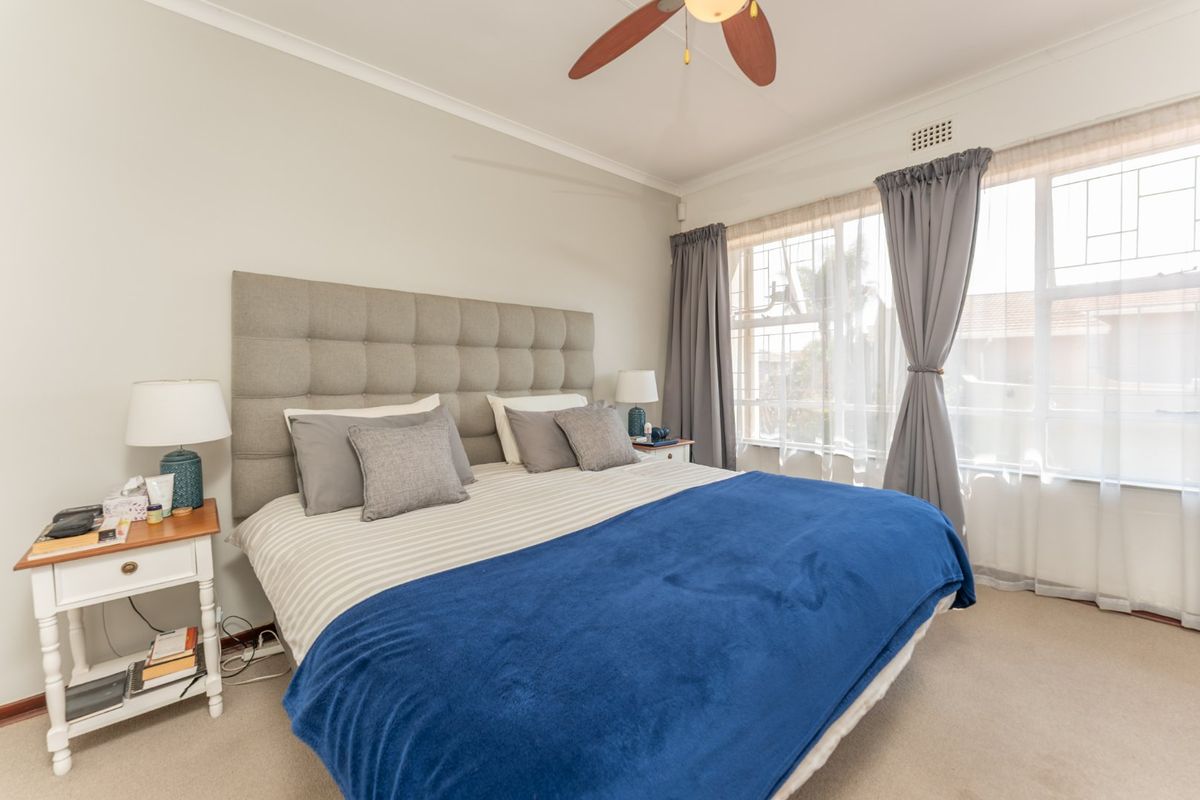 A well-maintained bedroom featuring neutral carpeting, a ceiling fan, and large windows that provide ample natural light.