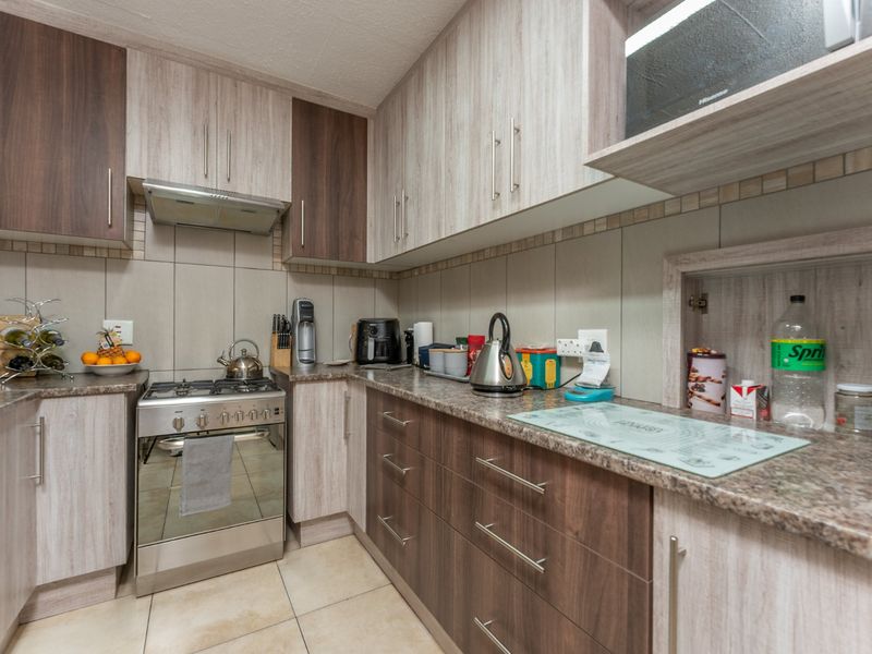 A functional kitchen featuring two-tone cabinetry, granite-look laminate countertops, a gas stove with extractor fan, and neutral tiled backsplash and flooring.