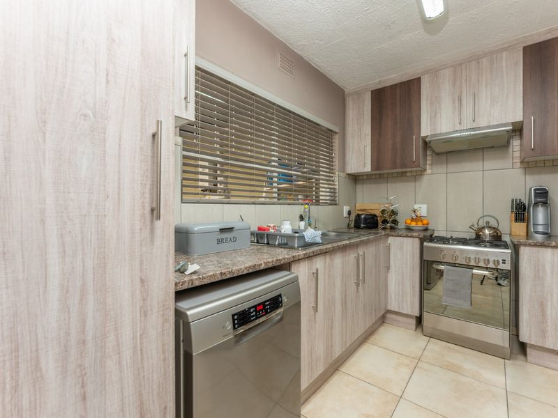 Functional kitchen featuring light wood-look cabinetry, stone-patterned countertops, stainless steel gas stove with extractor, and tiled flooring.