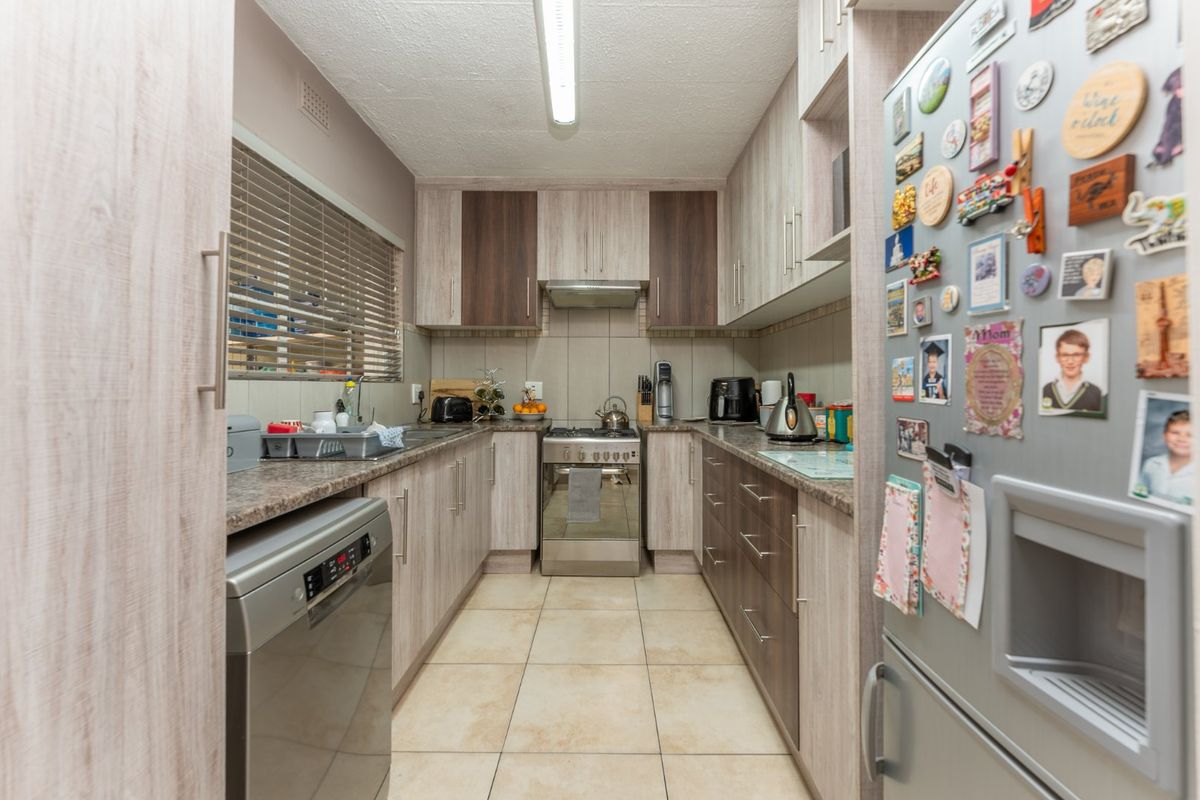 A functional galley-style kitchen featuring laminate cabinetry, granite countertops, a stainless steel gas stove, and tiled flooring.