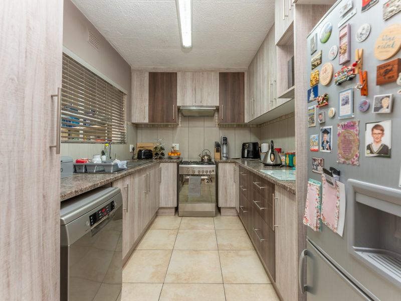 A functional galley-style kitchen featuring laminate cabinetry, granite countertops, a stainless steel gas stove, and tiled flooring.