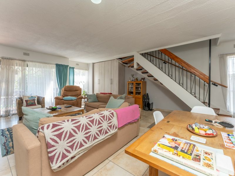 Open-plan living and dining area featuring tiled floors, a staircase with wrought iron balustrade, and sliding glass doors leading to the exterior.