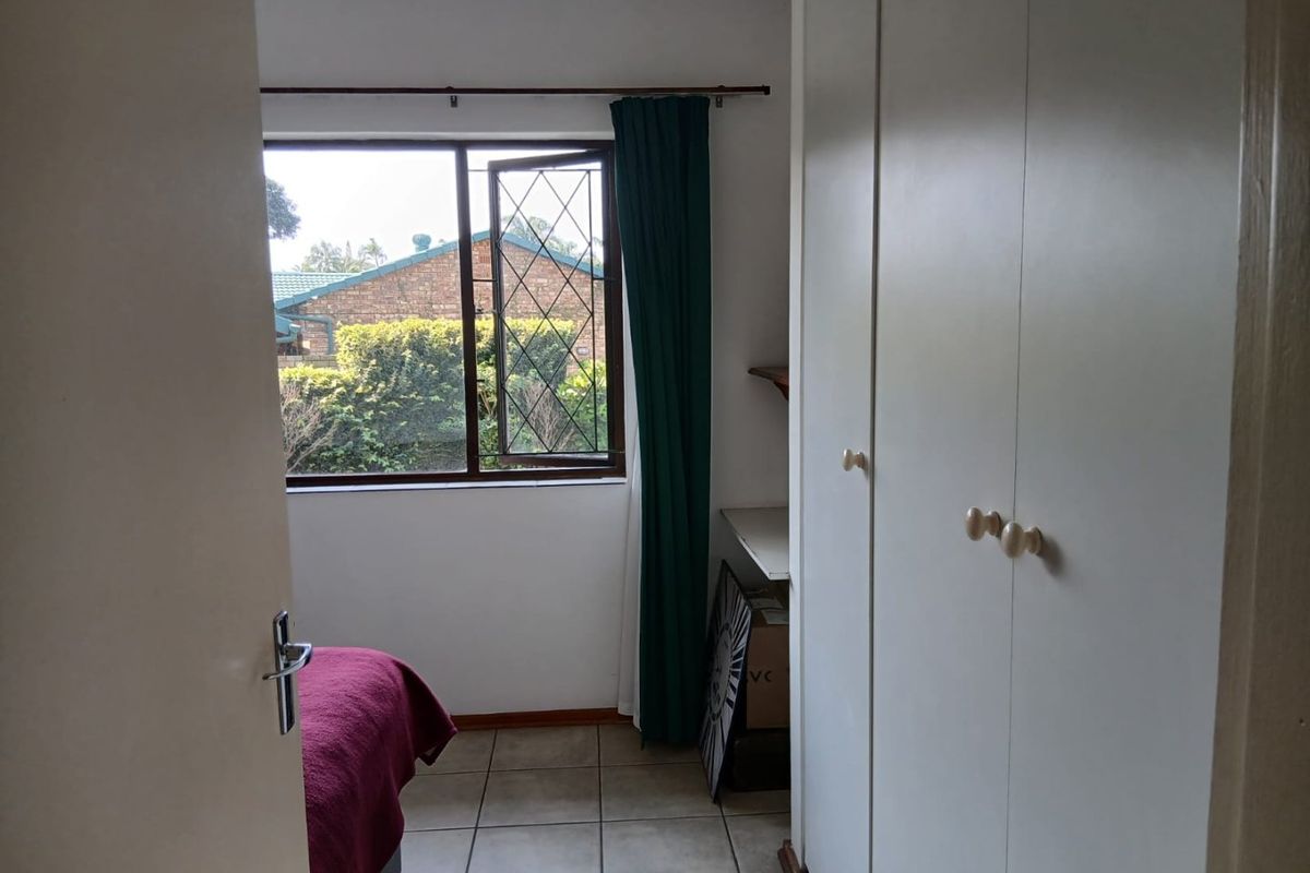A bedroom featuring tiled flooring, built-in cupboards, and a leaded glass window overlooking the exterior garden area.