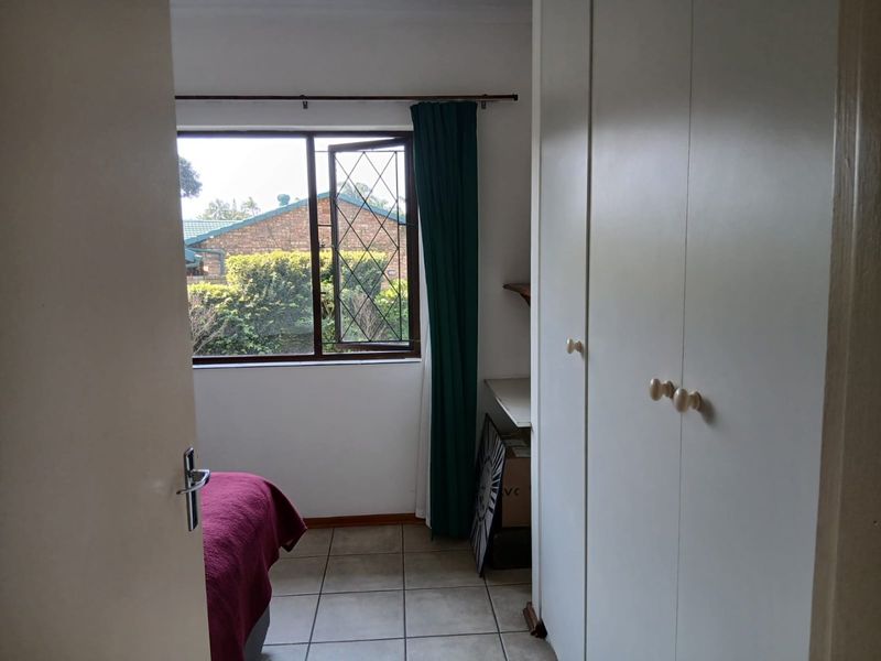 A bedroom featuring tiled flooring, built-in cupboards, and a leaded glass window overlooking the exterior garden area.