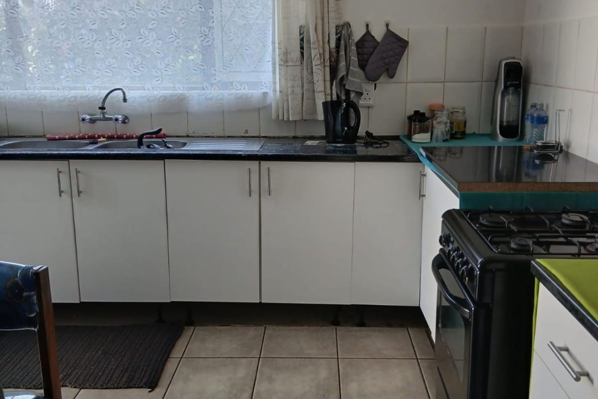 Functional kitchen featuring white cabinetry, tiled splashbacks, a double sink, and a gas stove with tiled flooring throughout.