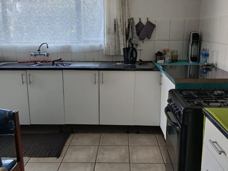 Functional kitchen featuring white cabinetry, tiled splashbacks, a double sink, and a gas stove with tiled flooring throughout.