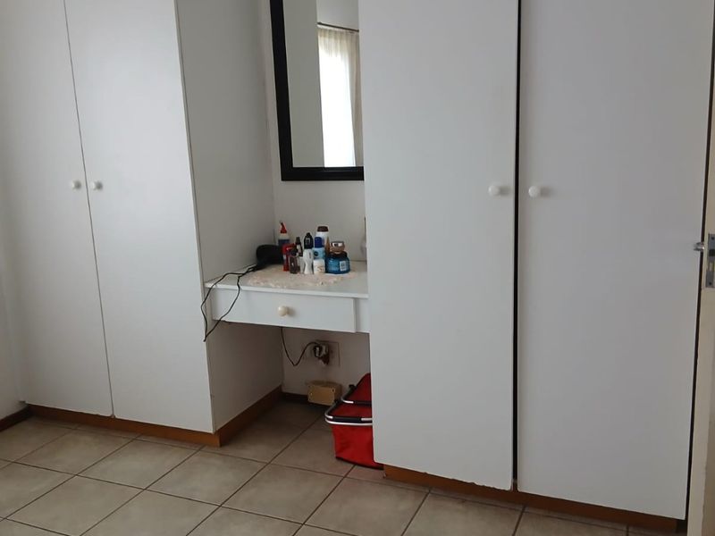 Bedroom featuring built-in cupboards with an integrated vanity unit and neutral tiled flooring.